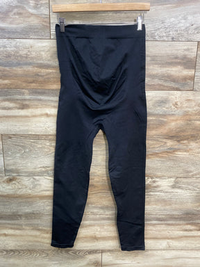 Black high-waisted maternity leggings hanging on wooden hanger, wood floor background