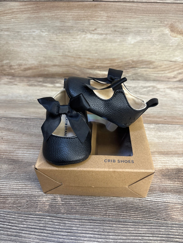 Black baby crib shoes with bows, soft sole, in box on wood floor