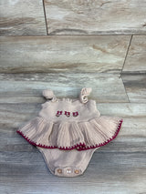 Flat lay of beige Nicole Miller knitted baby bodysuit showcasing embroidered flowers, ruffled skirt and maroon-trimmed hem on wood floor