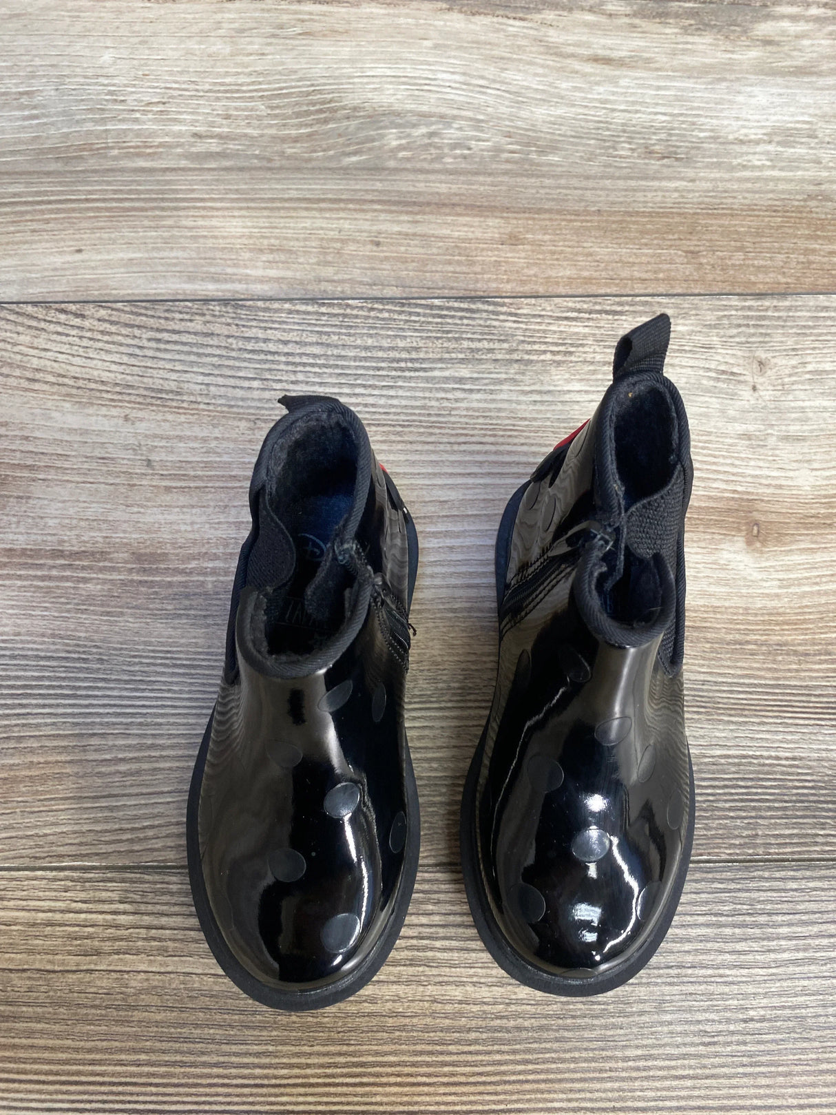 Pair of black kids' rain boots with polka dots on wood floor