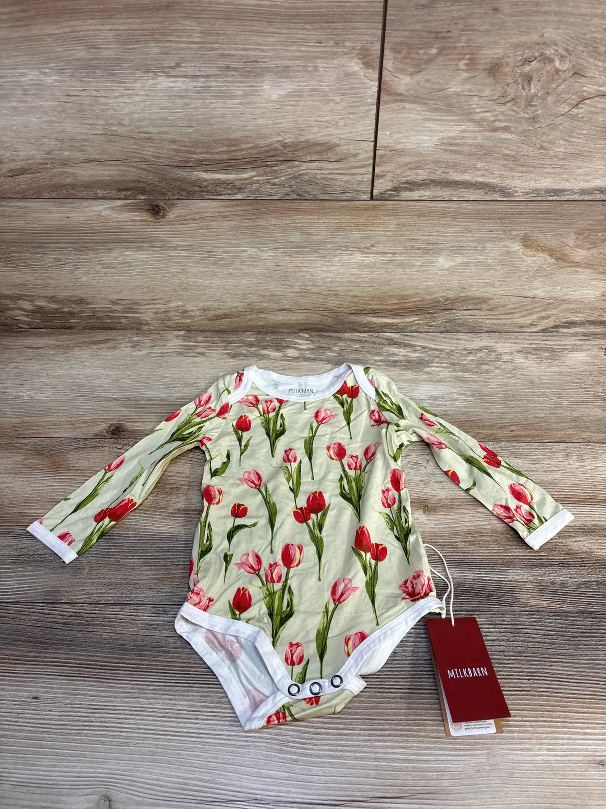 MILKBARN baby onesie with red tulip print, long sleeves, and snap closure on wood floor