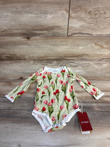 MILKBARN baby onesie with red tulip print, long sleeves, and snap closure on wood floor