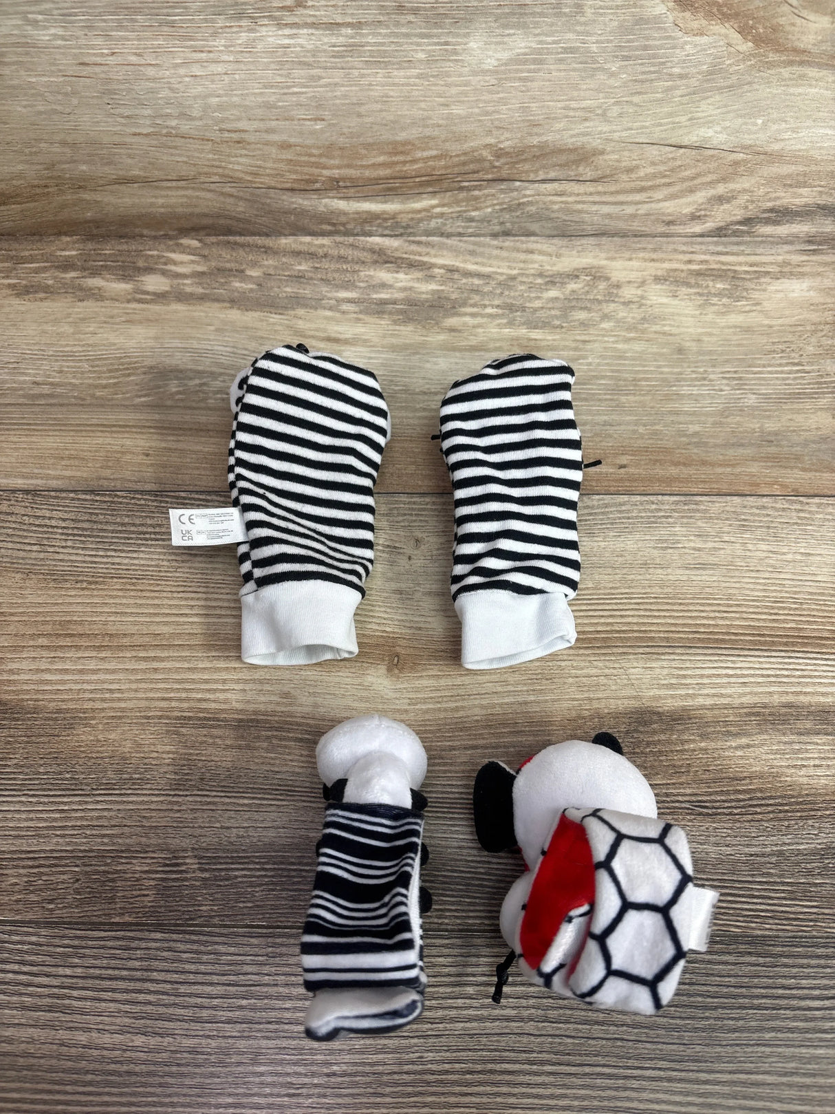 Top-down view of Infinno high-contrast baby wrist rattles and foot finders with black-and-white striped mittens on wood