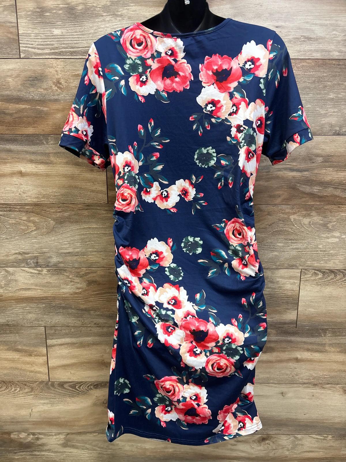 Front view of Musidora floral maternity ruched dress showcasing navy fabric and short sleeves with a wood-look background