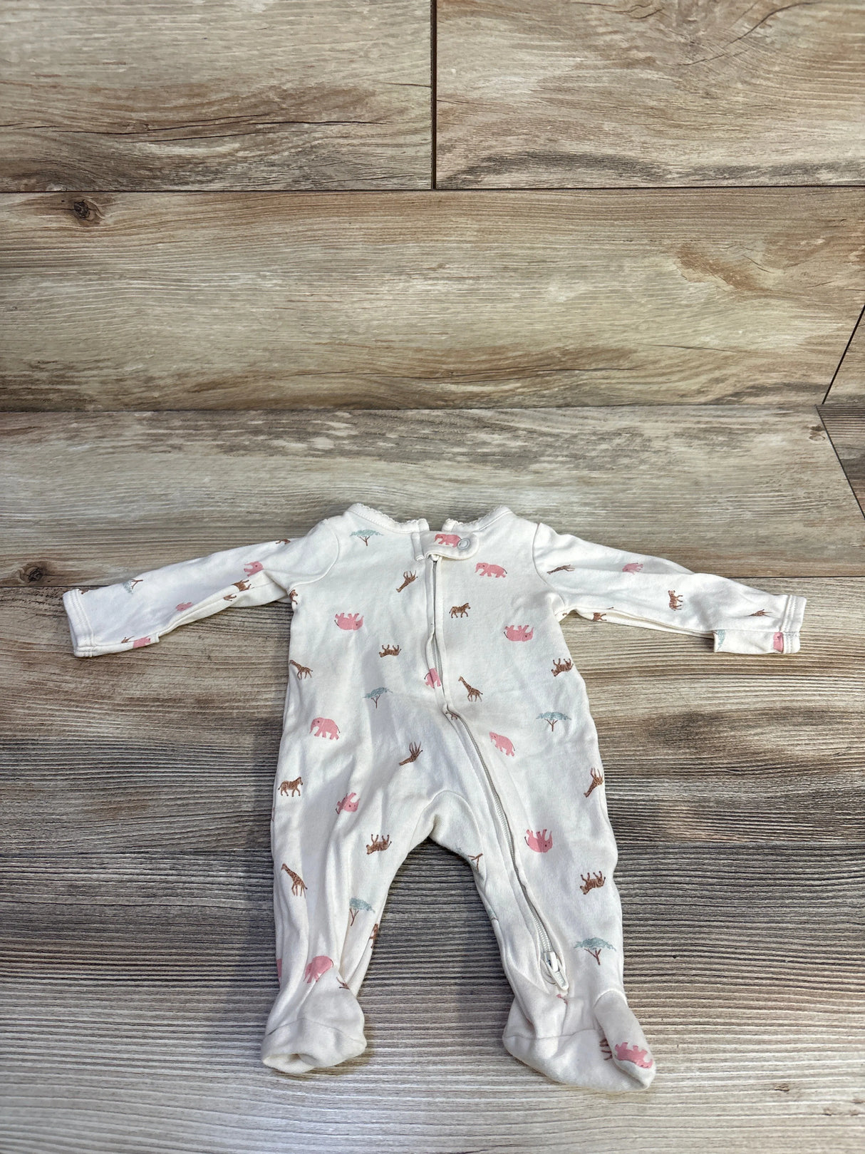 Flat lay of ivory preemie footed sleeper with pink animal print and front zipper on wood background