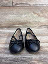 Front view of Cat and Jack Nora black toddler slip-on ballet flats showing bow detail and elastic strap on wood floor background
