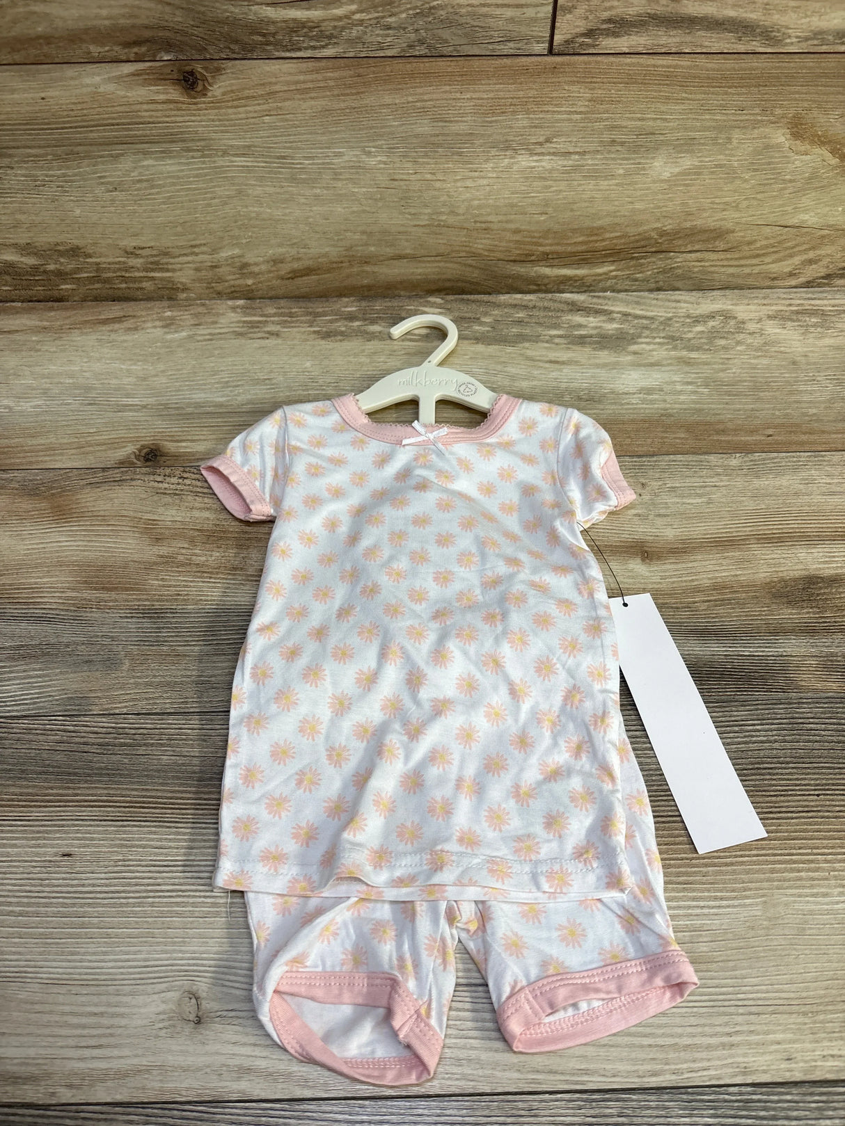 Front flat lay of Milkberry 2-piece bamboo baby pajama set (12 months) showcasing peach daisy print and pink trim on wood floor background