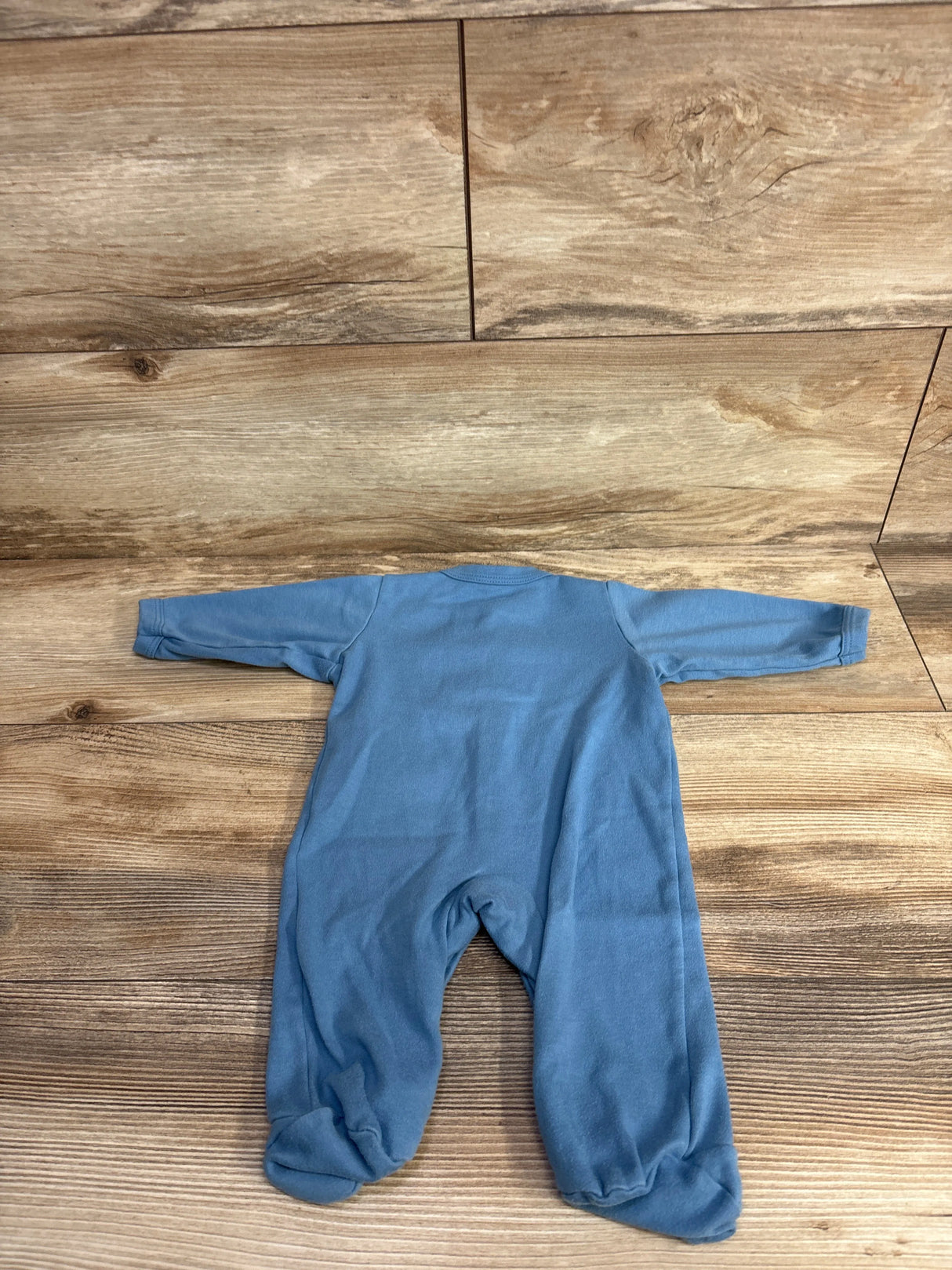 Blue long-sleeve baby footed pajamas laid flat on wooden floor background
