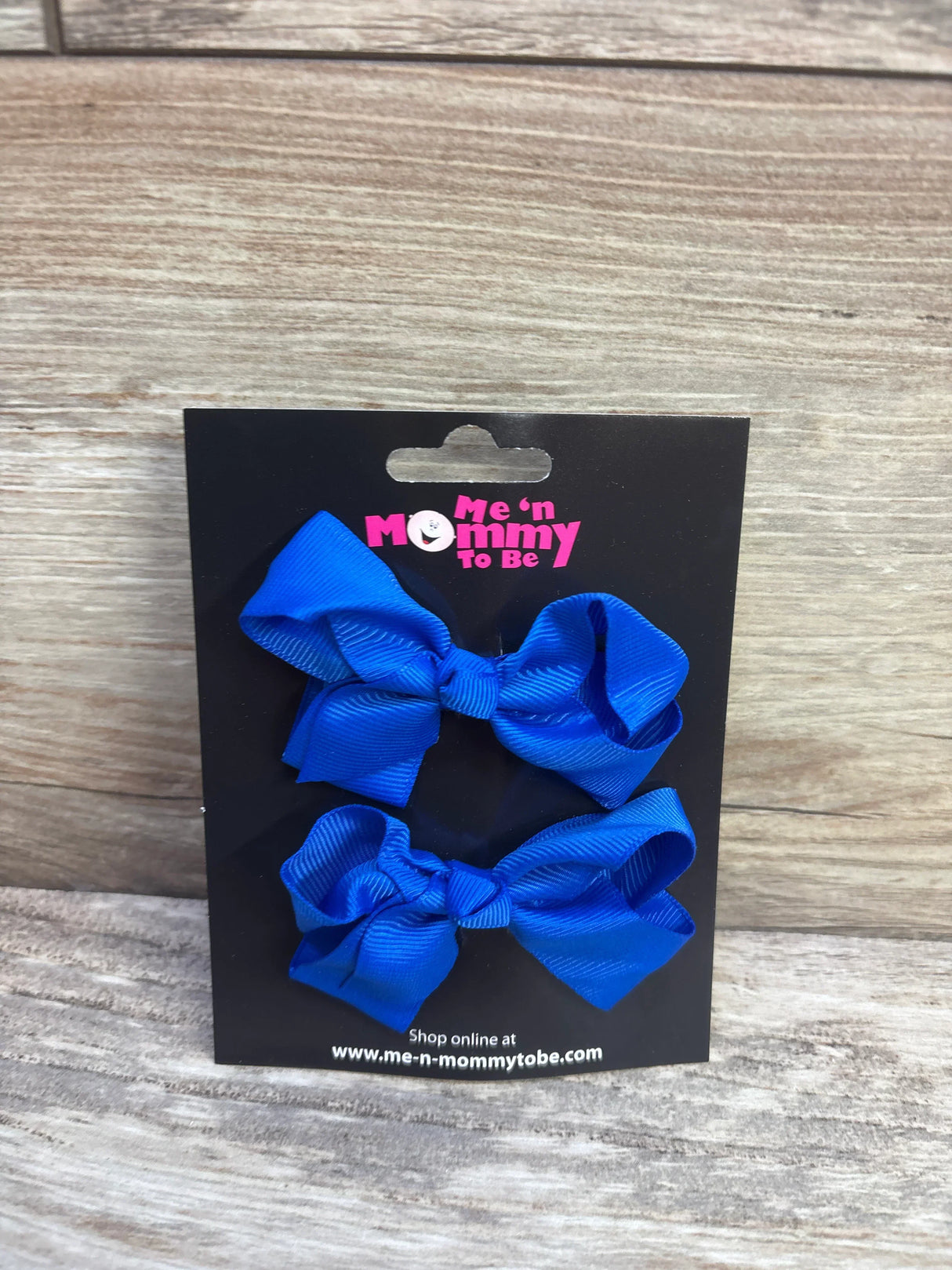 Front view of two royal blue grosgrain hair bows on a black Me n Mommy To Be display card against a light wood background
