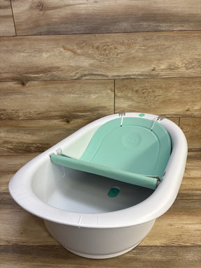 Three-quarter top view of Frida Baby 4-in-1 bath tub with mint-green recline insert and visible drain plug on wood floor