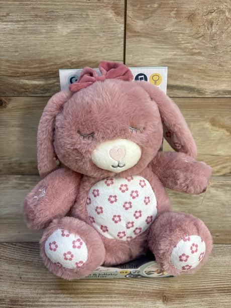Front view of NEW DreamGro Lights and Lullaby Soother pink plush bunny with floral belly and ear bow on wood plank floor
