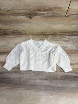 White knit baby cardigan with diamond pattern and buttons on wooden floor