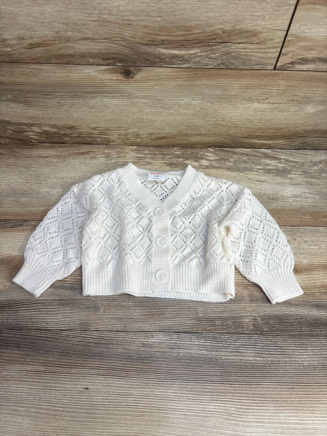 White knit baby cardigan with diamond pattern and buttons on wooden floor