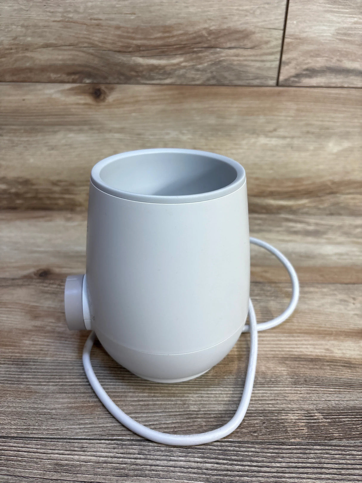 White electric baby bottle warmer on wood floor, cord coiled beside