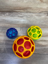 Top view of Bright Starts Oball stackable hollow balls (orange-red, yellow-green, blue) on wood background