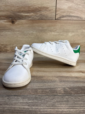 White kids sneakers with green heel tab on wood floor, gently used children's shoes