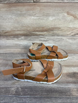 Angled view of Lucky Brand Kiara brown toddler sandals (size 8C) showing braided leather straps, ankle buckle and cork footbed on wood background
