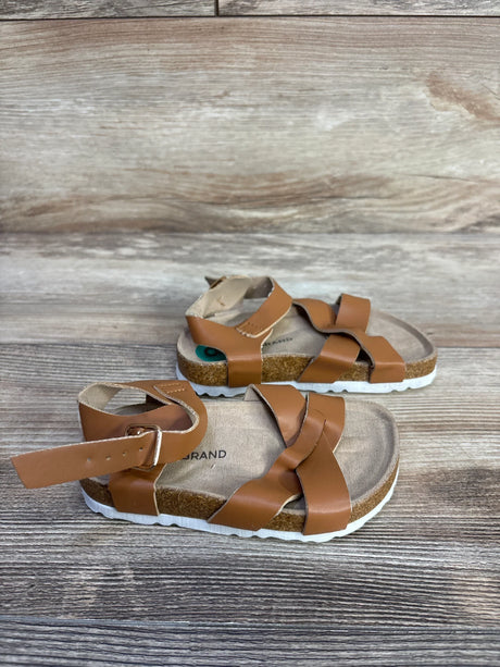 Angled view of Lucky Brand Kiara brown toddler sandals (size 8C) showing braided leather straps, ankle buckle and cork footbed on wood background