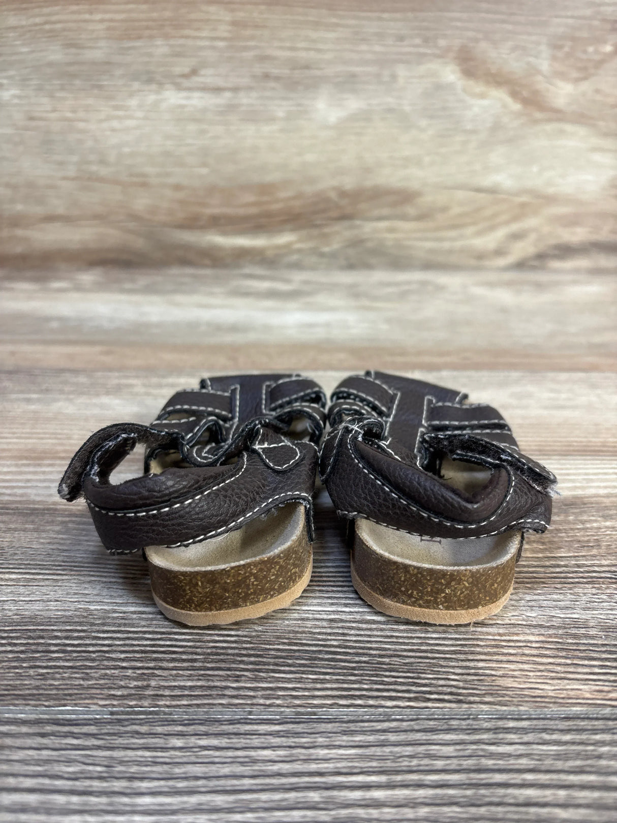 Brown toddler sandals with Velcro straps and cork soles on wood background