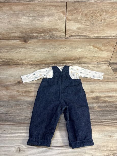Flat-lay of infant dark denim overalls with rolled cuffs paired with ivory long-sleeve shirt with small animal print on wood background