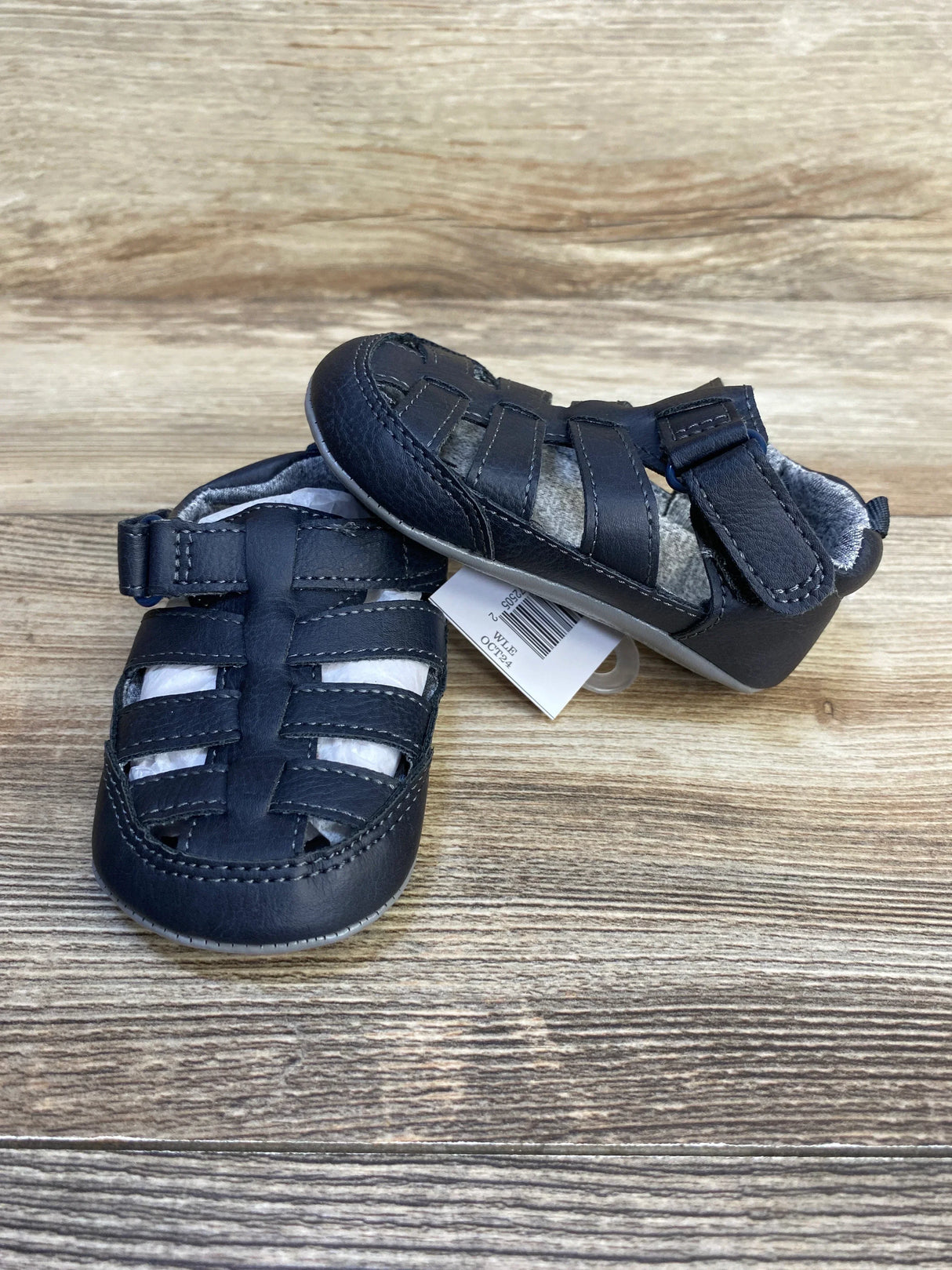Front and side view of Just One You navy fisherman sandals size 4/5C 12-18M, woven toe straps and velcro tab on wood background