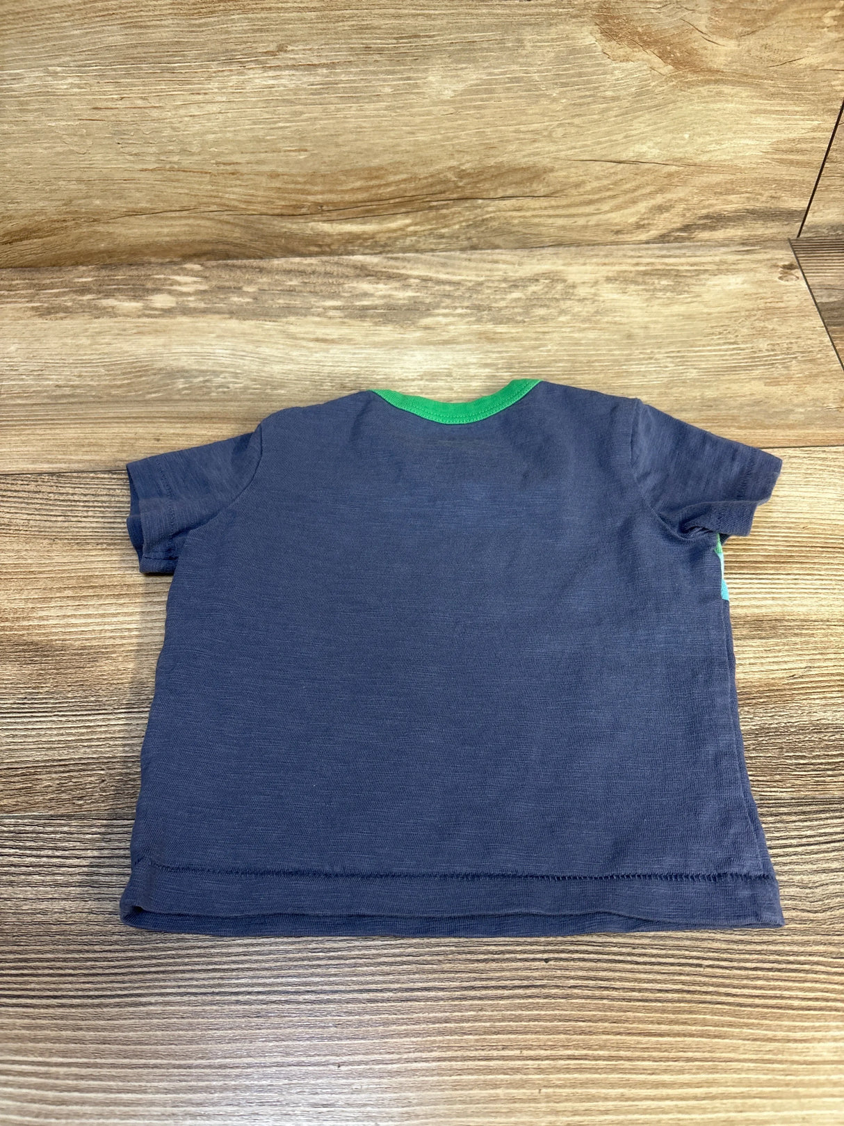 Navy blue short sleeve toddler t-shirt with green neckline on wood background