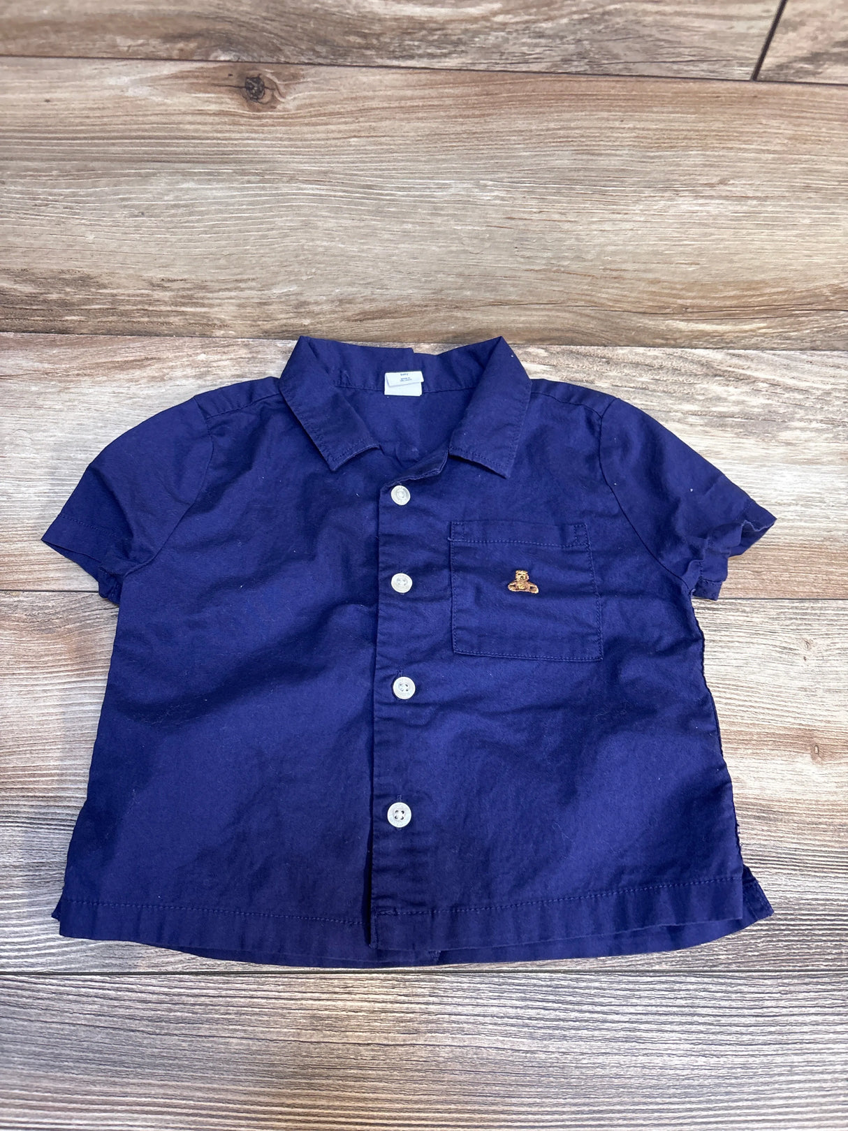Short sleeve navy blue button-up toddler shirt with chest pocket on wood background