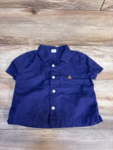 Short sleeve navy blue button-up toddler shirt with chest pocket on wood background