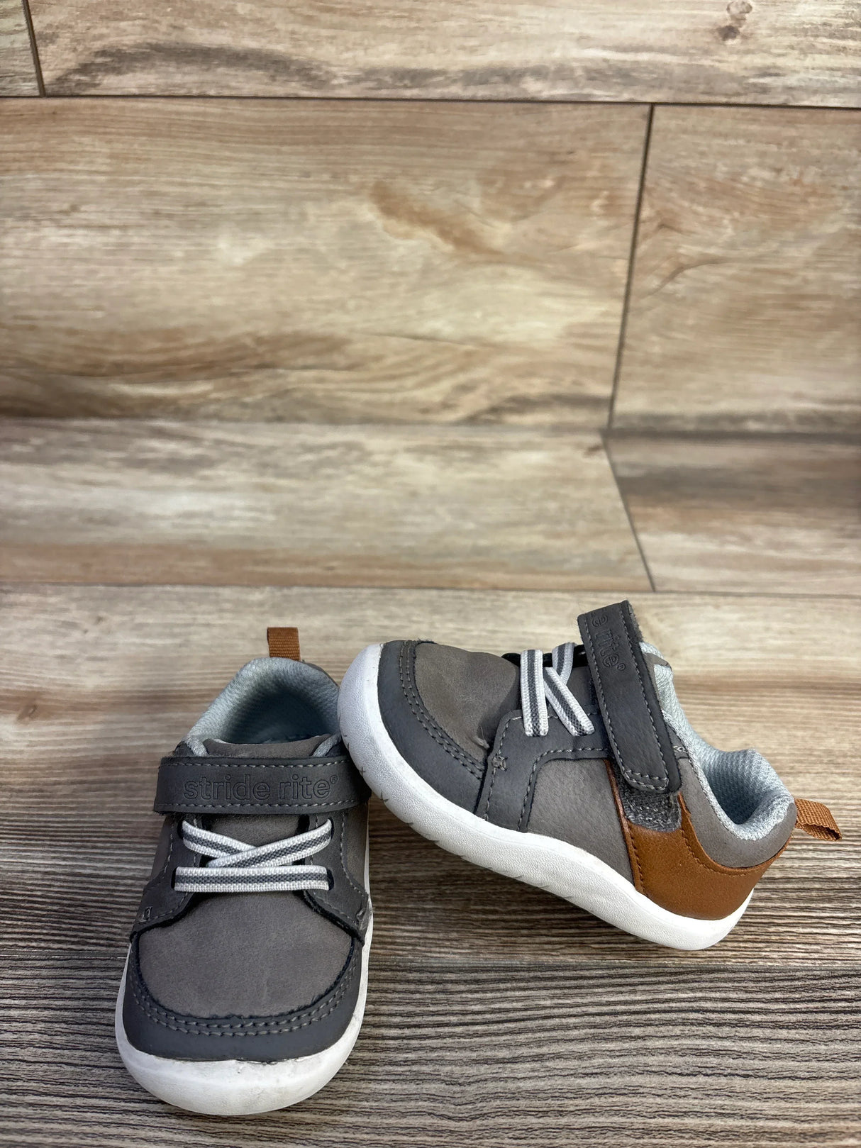 Front view of Munchkin by Stride Rite sneaker, grey and brown, velcro strap reading stride rite, white sole on wood floor