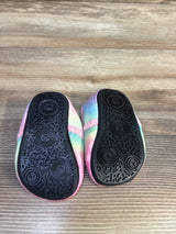 Bottom view of unicorn toddler slippers size 5C showing black textured rubber soles and pastel rainbow plush uppers on wood floor