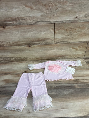 Pink baby girl outfit with lace cuffs and floral decoration, set on wooden surface