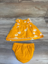 Flat lay of yellow baby dress and matching bloomers showing white floral print and ruffled sleeves on wood floor