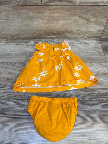 Flat lay of yellow baby dress and matching bloomers showing white floral print and ruffled sleeves on wood floor