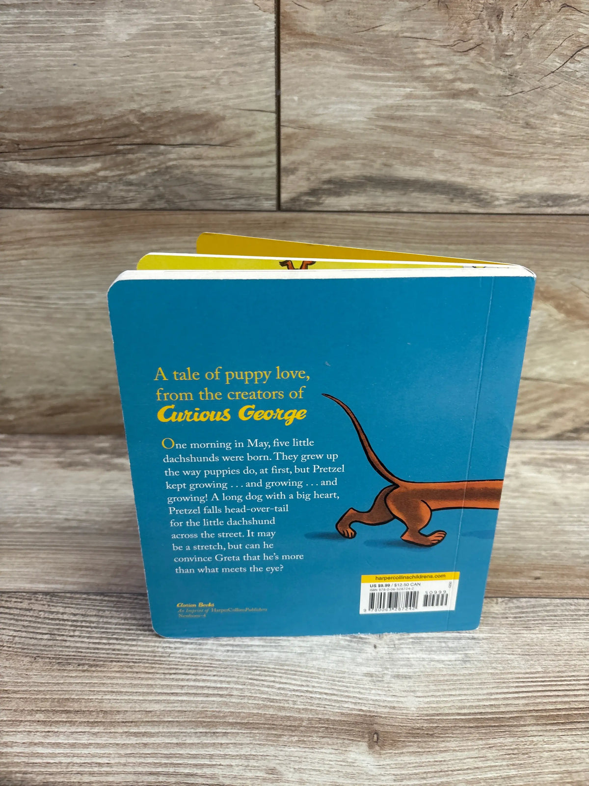 Back view of Pretzel board book showing a blue cover with a dachshund illustration and story text on a wood surface