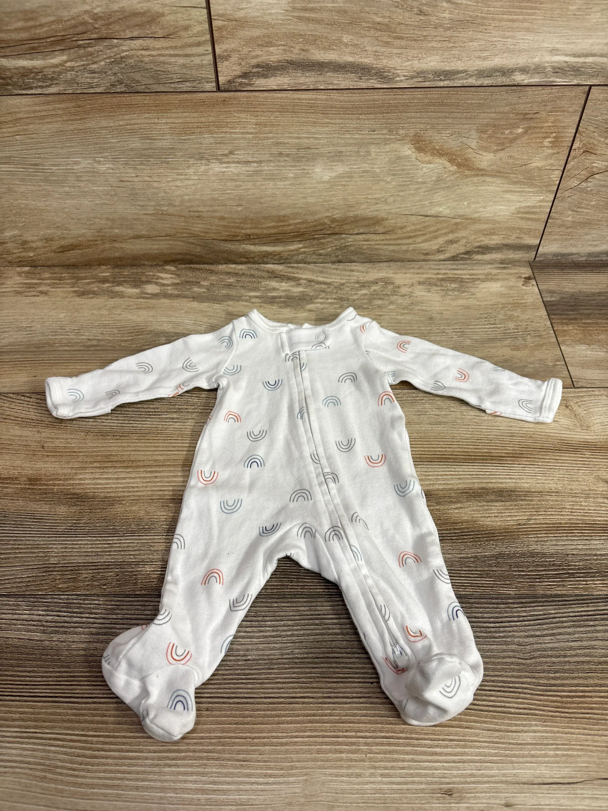 Flat lay of Simple Joys preemie white sleeper showing front zipper and multicolor rainbow print on wooden floor background