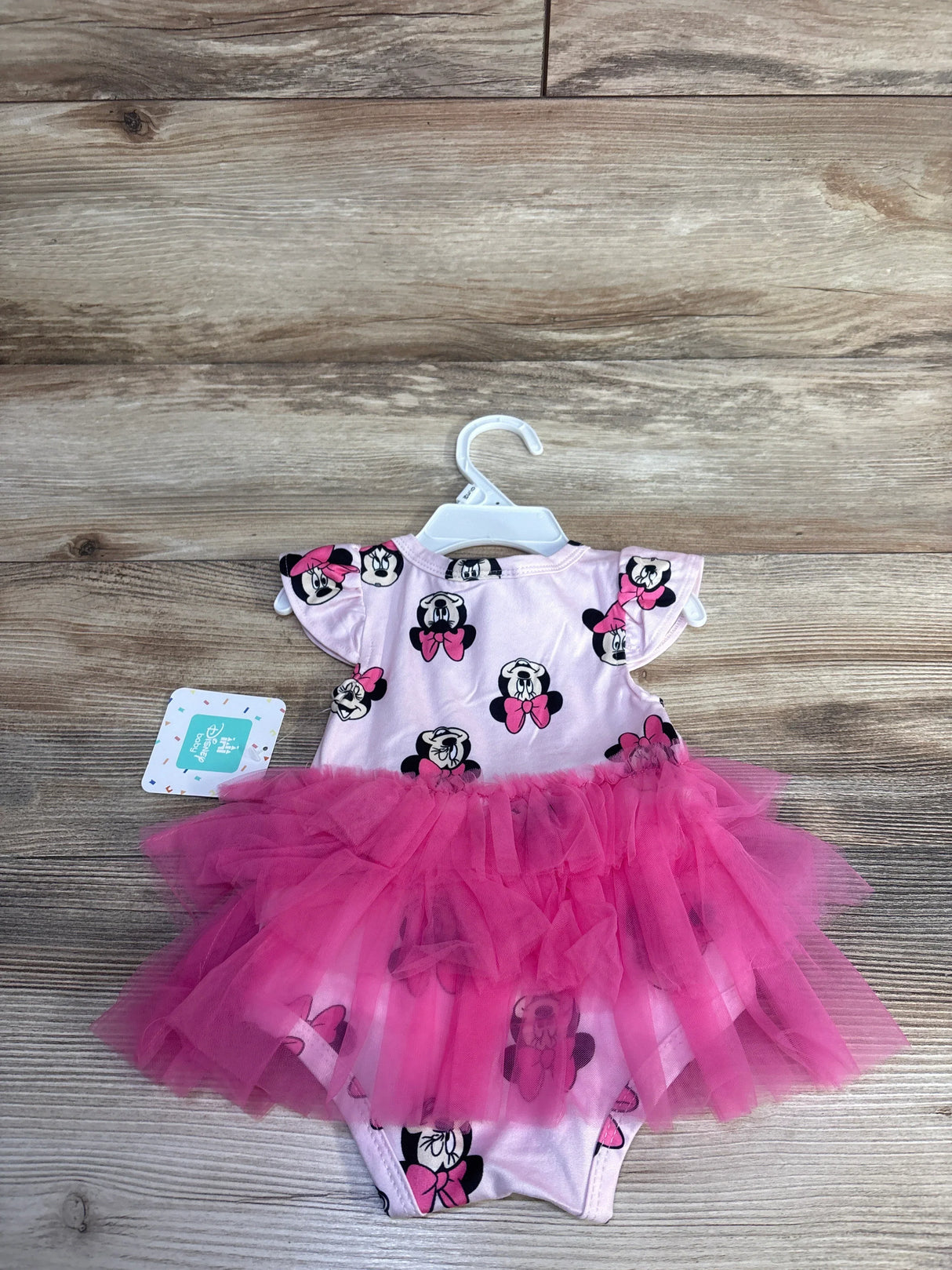 Front view of newborn pink Disney Minnie Mouse bodysuit with hot-pink tulle tutu on wood plank background