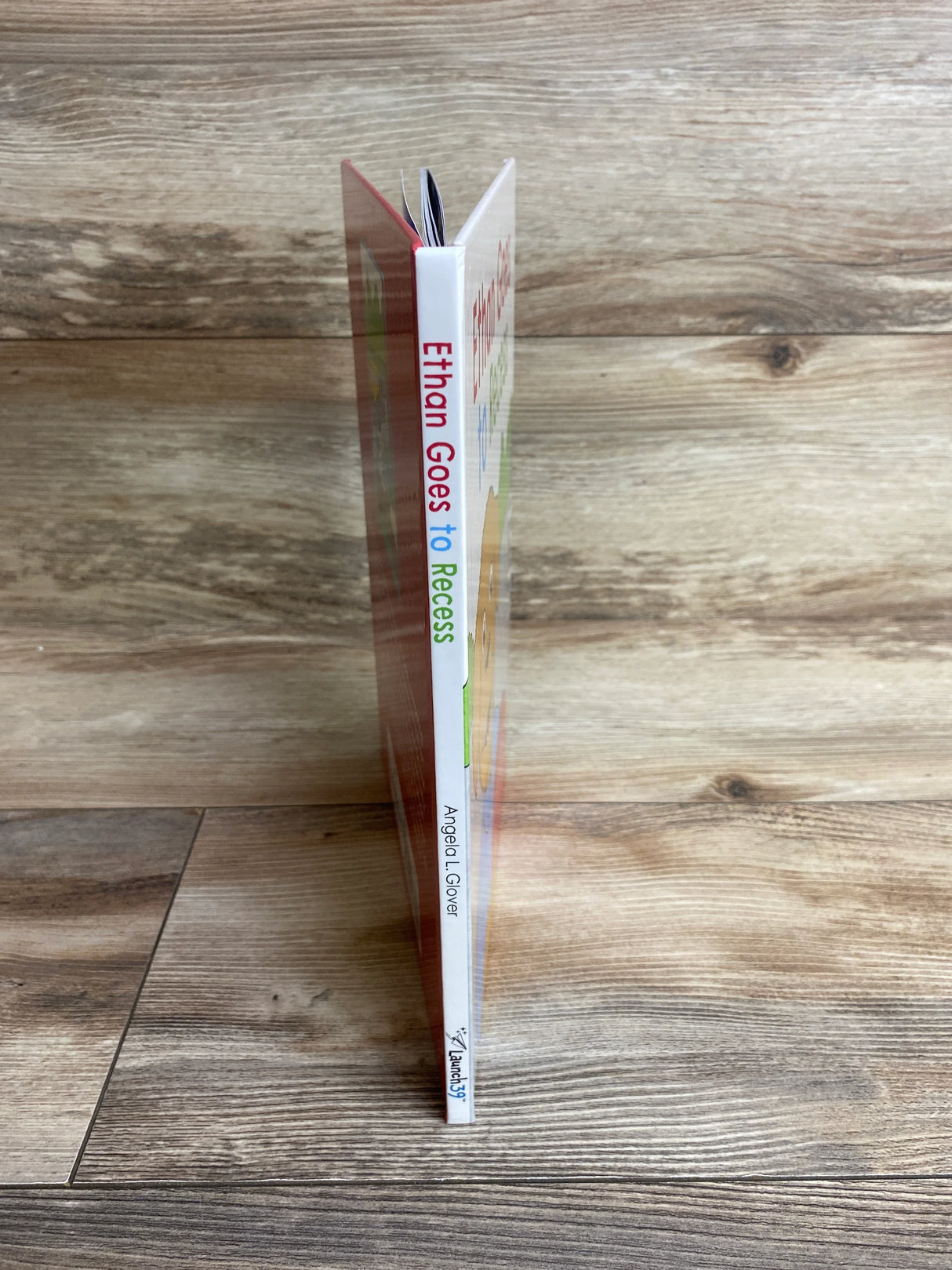 Children's book titled Ethan Goes to Recess by Angela L. Glover standing on wooden floor