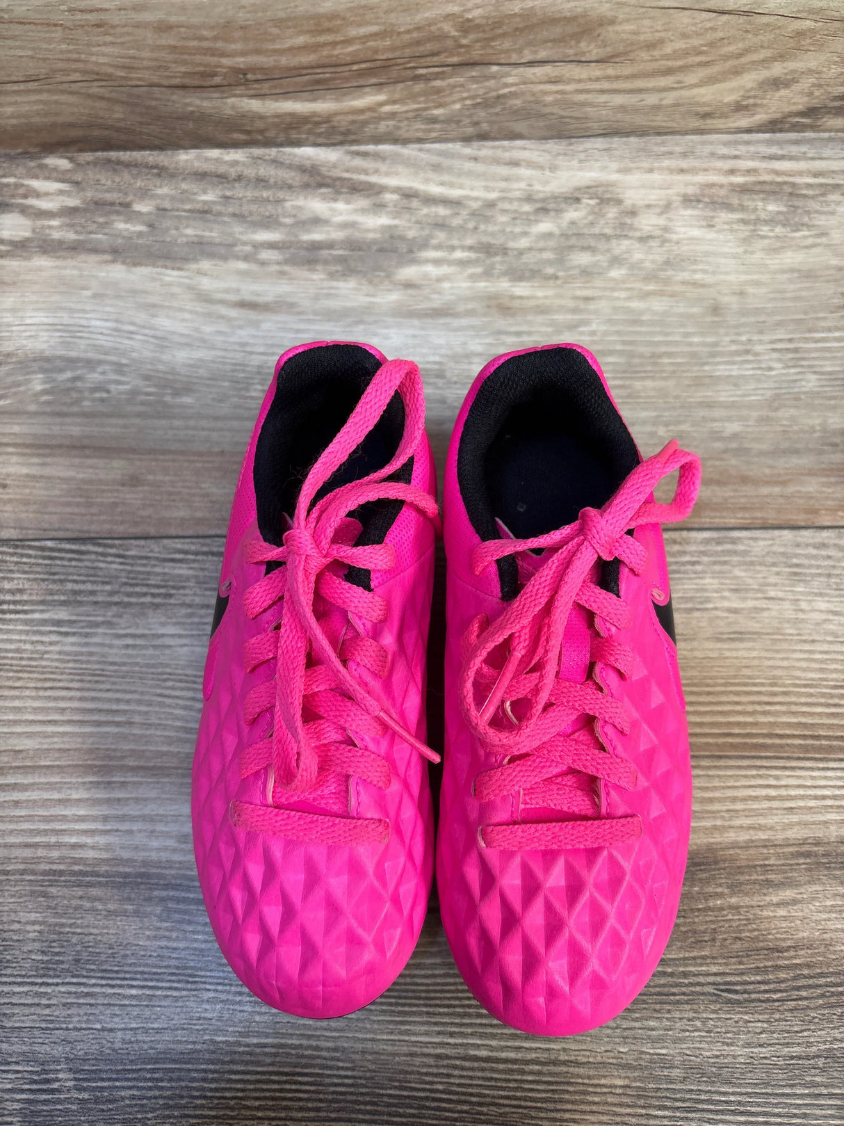 Bright pink kids' soccer cleats with black accents on wood floor