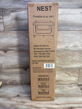 Front view of Dream On Me Nest portable playard box showing product illustration, child maximum weight 30 lbs warning and barcode on a wood floor background