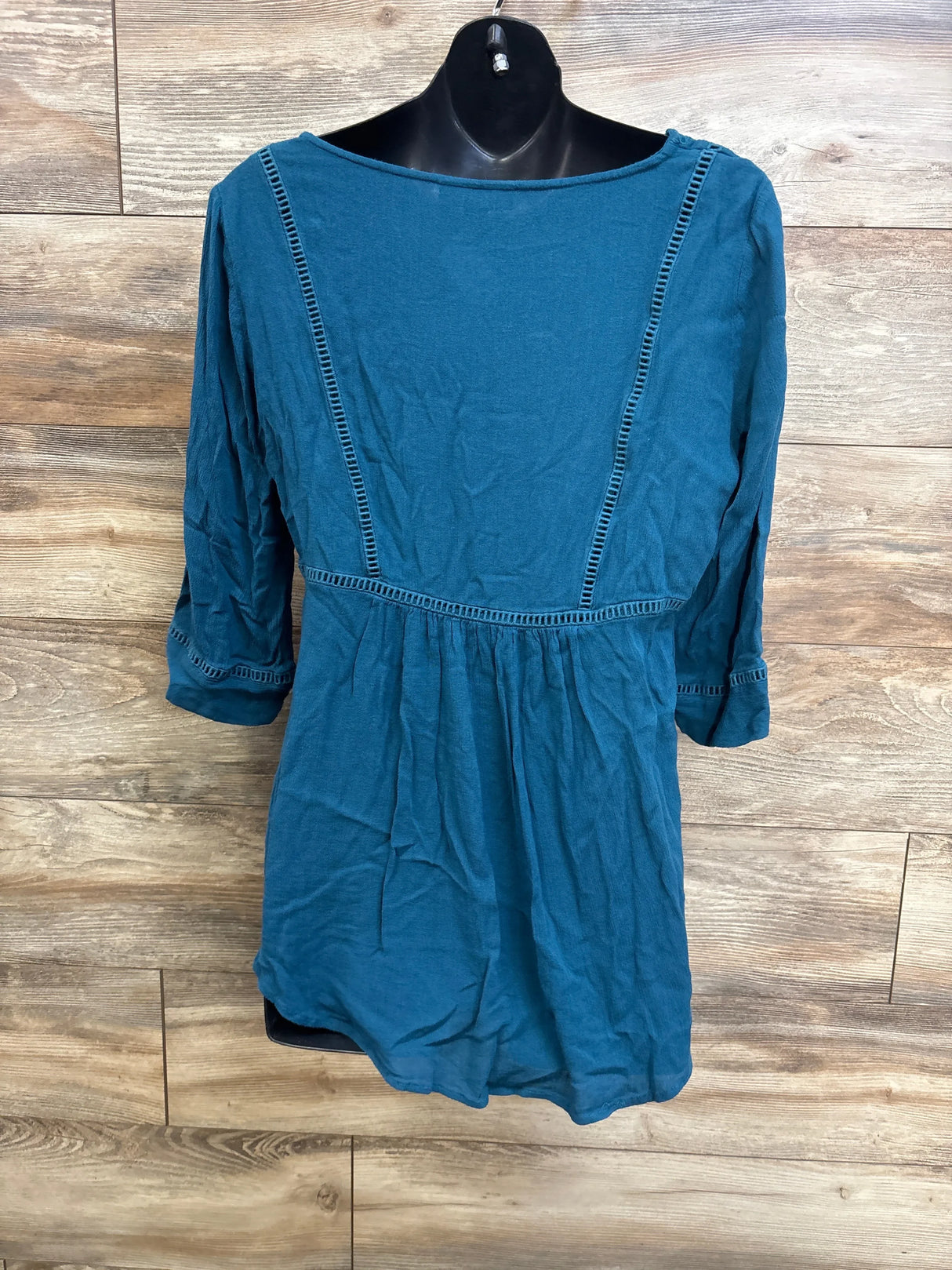 Front view of blue maternity lace top showing ladder lace trim, empire waist and three-quarter sleeves on a black mannequin against wood background