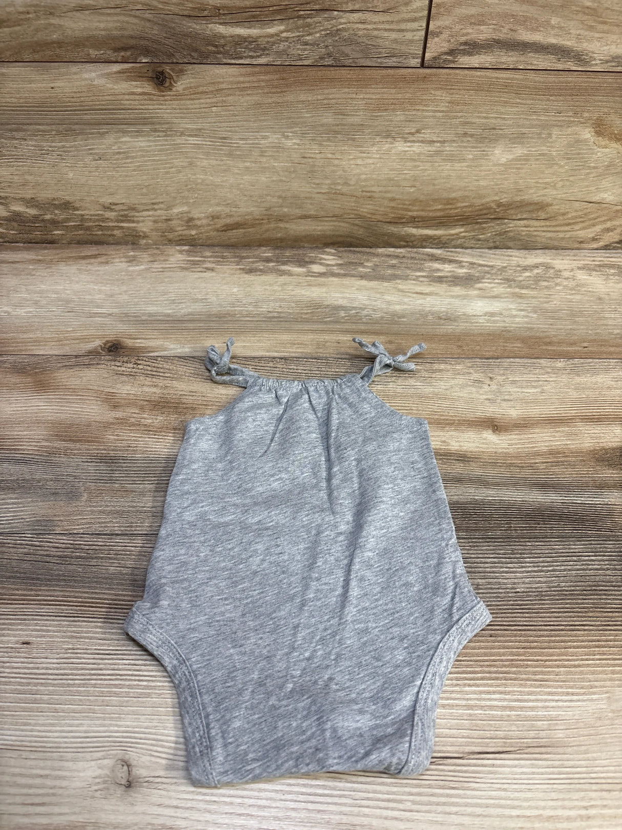 Flat lay of Okie Dokie grey 3M baby bodysuit showcasing knotted shoulder straps and heathered fabric on wood background
