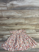 Laid-flat of girls' ivory short-sleeve tiered swing dress with pink-orange floral print, size 5T, on light wood background