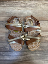 Toddler sandals with gold and brown straps on wood floor, MK logo pattern insole