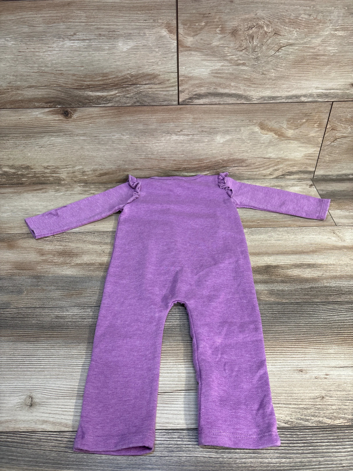 Purple baby onesie with ruffled shoulders, laid flat on wood floor. Soft knit, long sleeves, ideal for infants.