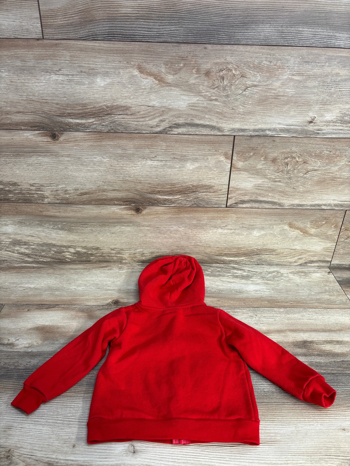 Red hooded sweatshirt laid flat on light wood floor with visible wood grain