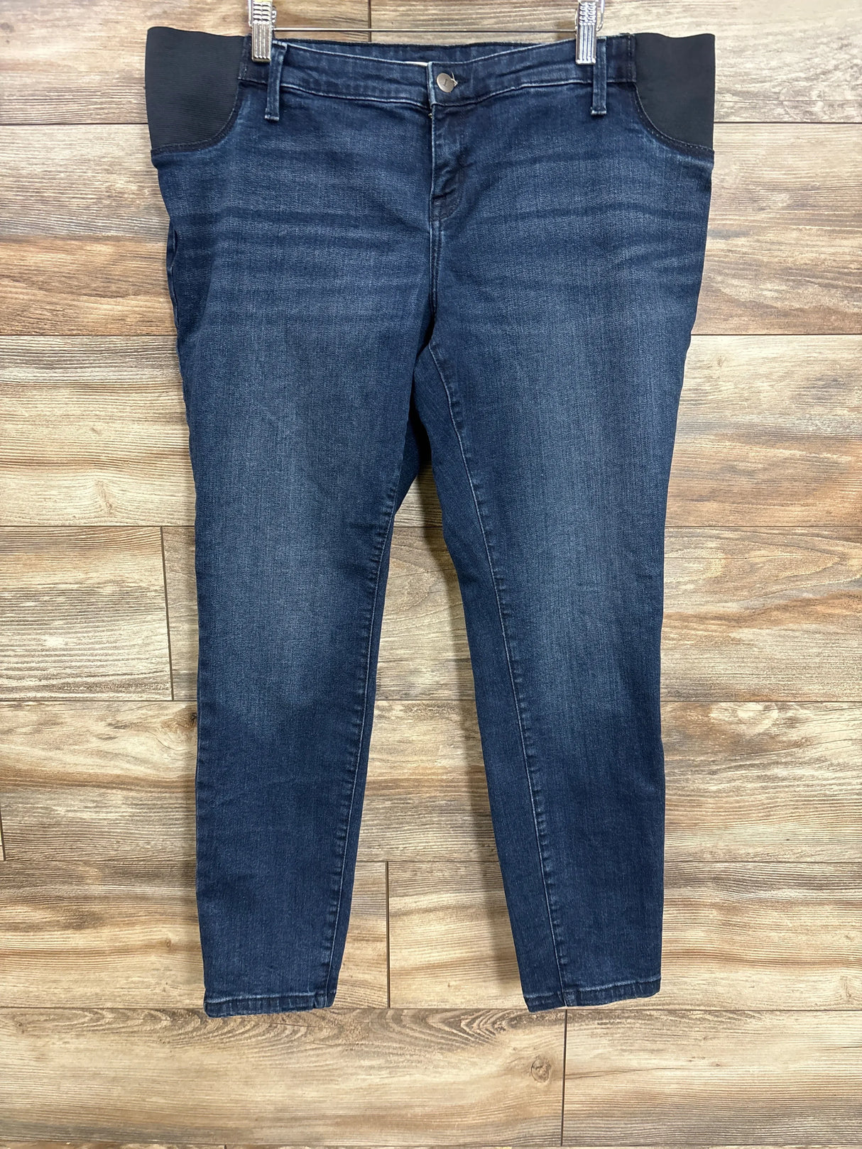 Flat lay of Isabel Maternity side panel skinny jeans in dark wash blue with black elastic side panels on wood plank floor