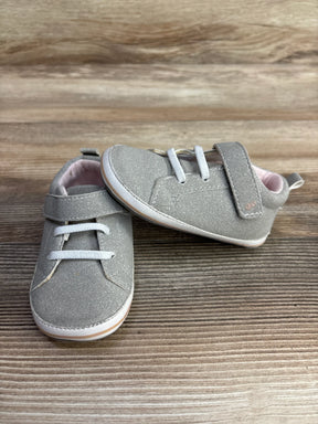 Pair of gray toddler shoes with white laces and Velcro strap on wooden surface