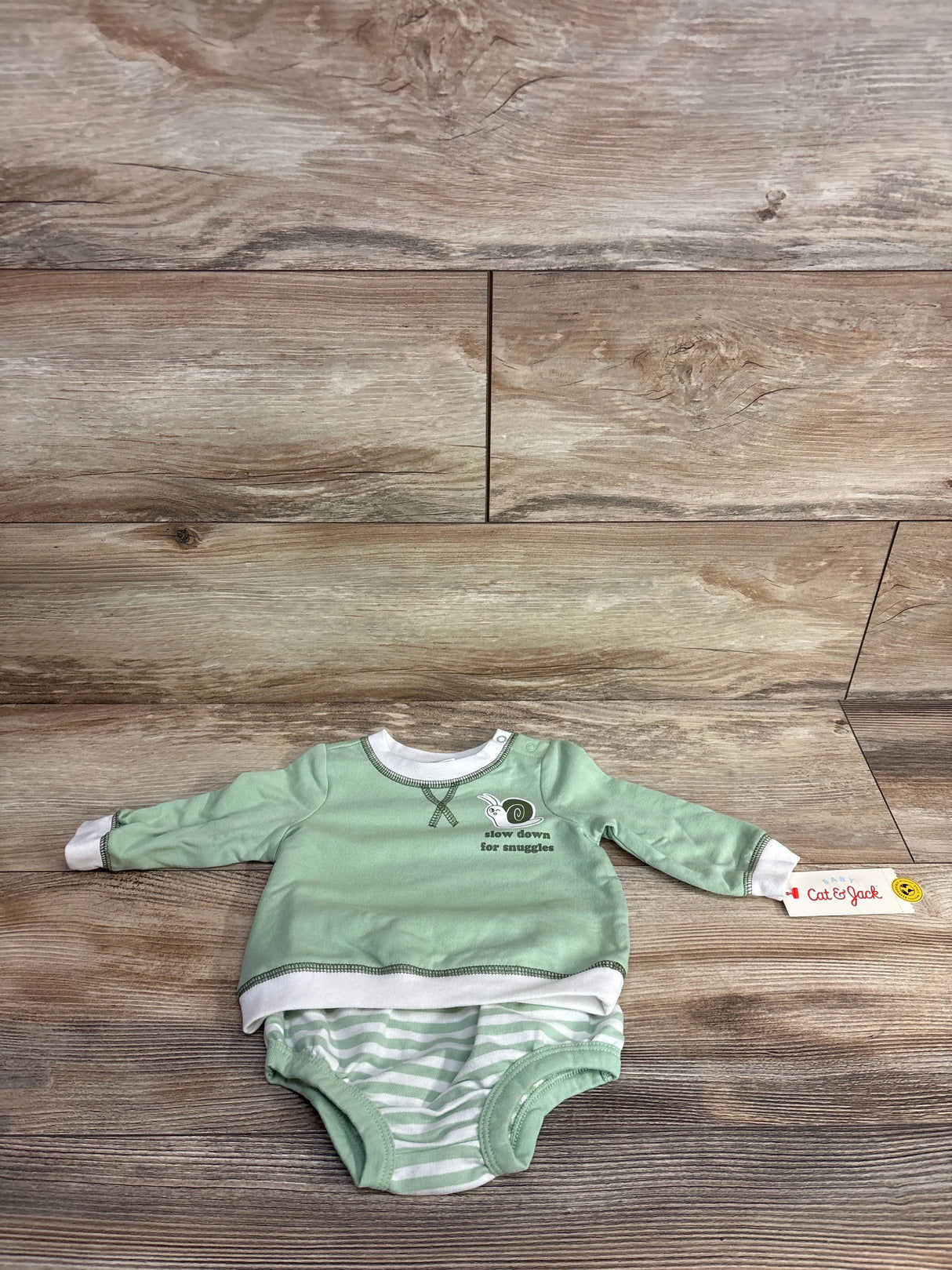 Mint green baby onesie with white striped bottom and snail graphic, laid on wood floor