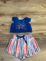 Flat lay of girls' patriotic 2-piece set: blue crop top with sequin star and red-white-blue striped shorts on wood background