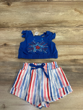 Flat lay of girls' patriotic 2-piece set: blue crop top with sequin star and red-white-blue striped shorts on wood background